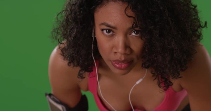 Close up of strong, determined young Black woman athlete staring at camera on greenscreen background. Fierce athletic female runner taking a break from running and breathing hard on green screen. 4k