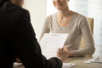 Close up image of contract document in businessman hands. Male entrepreneur reading text of business agreement, sitting at desk in front of smiling female business partner, studying conditions of deal