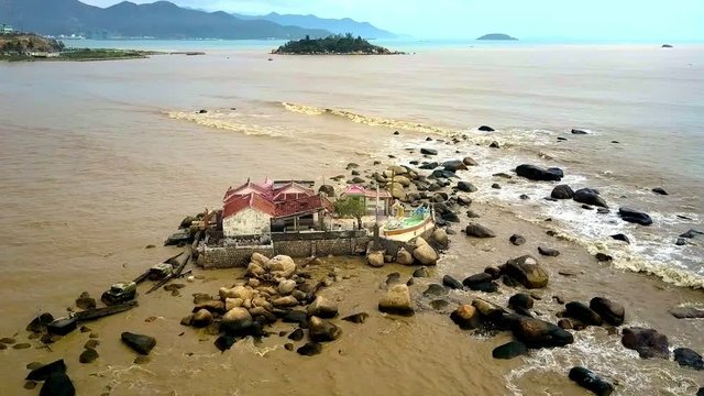 Waves Roll on Island with Temple against Hills City Upper View