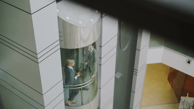 Tilt up of businesswoman and businessman colleagues talking in moving elevator and come out from it in modern business center