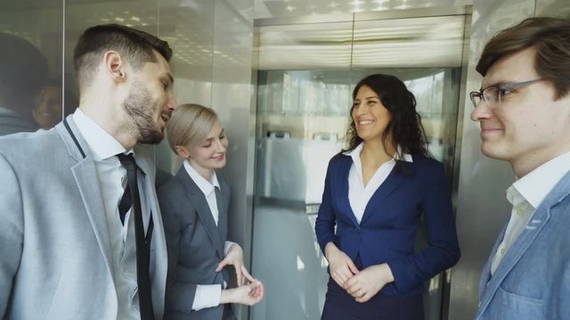 Tracking shot of Businesswomen and businessmen colleagues talking in moving elevator and come out from it and walking in hall in modern business center