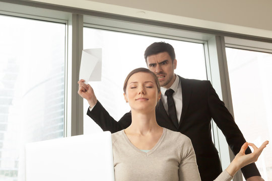 Funny young woman with peaceful facial expression meditating at workplace in office, angry boss with documents in hands arguing and screaming at background. Businesswoman resisting stress at work