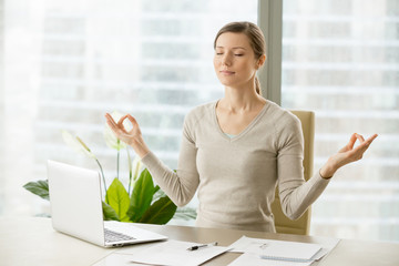 Relaxed woman meditating at workplace, practicing eastern spiritual practices for stress relief and...