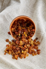 Ceramic bowl with golden raisins on light tablecloth, close-up, selective focus, vertical
