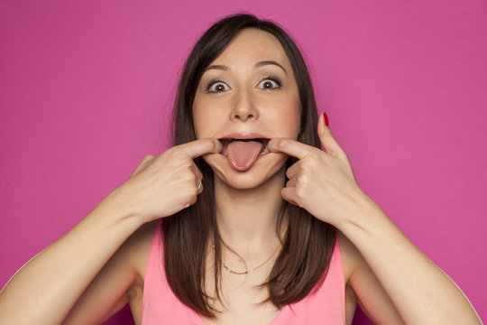 Young funny woman making silly faces on pink background