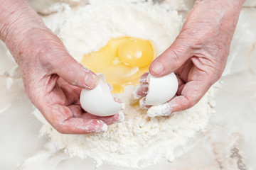Old hands break the egg into a flour on the table