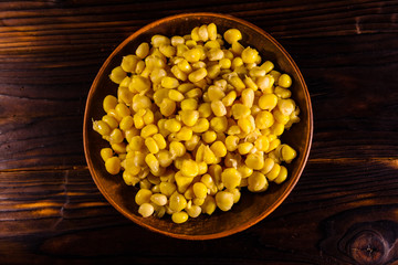 Ceramic plate with canned corn seeds on wooden table. Top view