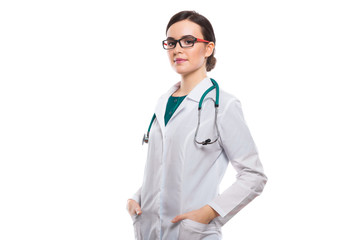 Young woman doctor with stethoscope holding her hands in pockets in white uniform on white background