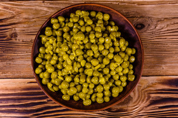 Ceramic plate with canned green pea on wooden table. Top view