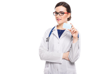 Successful young woman doctor with stethoscope with arms crossed showing business card in white uniform on white background