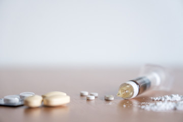 Heroin syringe needle wih heoin, cocaine powder and pills on the table.