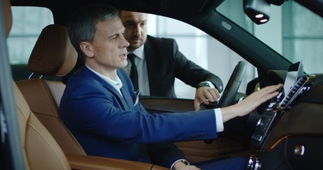 Side view of seller standing at window and showing options to adult businessman using car computer.