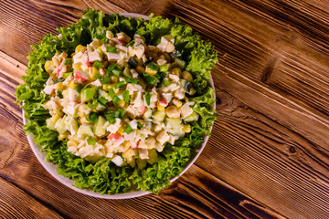 Ceramic plate with salad from crab sticks on wooden table. Top view