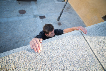 Young man hanging on wall on hands and trying to climb up while doing parkour.  
