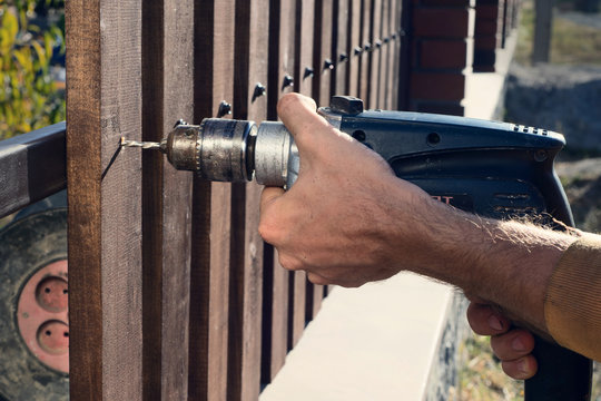 Man hands drilling wooden fence to metal construction. Building a wooden fence with a drill and screw. Close up of his hand and the tool in a DIY concept.