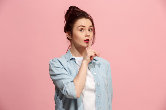 The young woman whispering a secret behind her hand over pink background