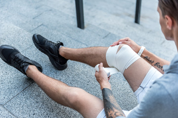 Top view close up man bandaging leg on floor outdoor. Injury concept