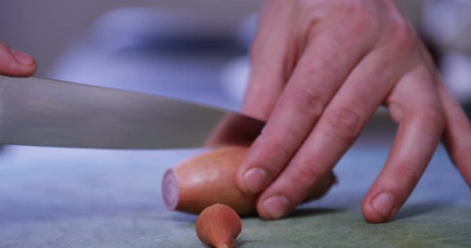 4K Close up on the hands of a skilled chef cutting a shallot on chopping board