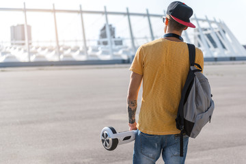 Modern teenager keeping gyroscope in arm while going outdoor. He turning back to camera. Copy space