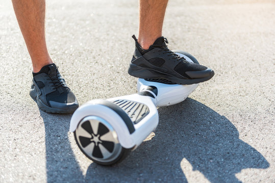 Close up boy leg standing on hoverboard while another situating on asphalt. Digital device concept