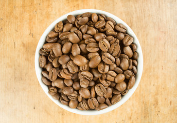 Fototapeta premium Light roast brown coffee beans in a white bowl on a wooden table top