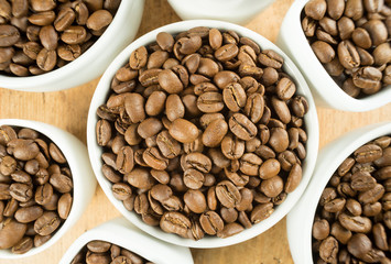 Lightly roasted brown coffee beans in white cups on a wooden table top