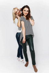 Two modern girls have fun posing in a white studio