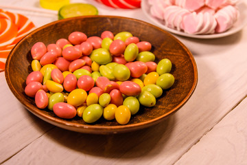 Ceramic plate with colored candies, lollipops and marshmallows on a wooden table