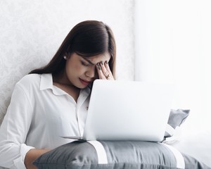 Asian woman  working with laptop in bedroom,she's feeling unwell.