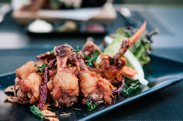 Thai style deep fried chicken wings, chicken drums with herbs, garlic and vegetable on black plate