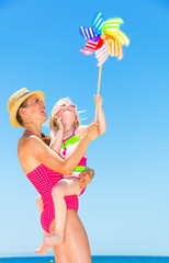 mother and child on seashore playing with colorful windmill toy
