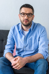 Obraz premium portrait of man in eyeglasses sitting on sofa and looking at camera
