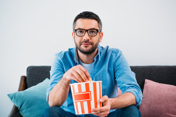 portrait of man in eyeglasses with popcorn watching tv