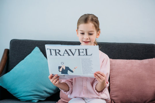 portrait of cute child reading travel newspaper while resting on sofa