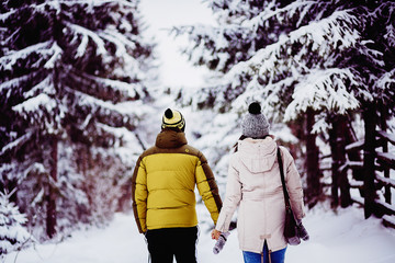 Look from behind at couple walking in winter clothes around the forest covered with snow