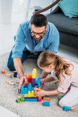 little daughter and father playing with colorful blocks together on floor at home