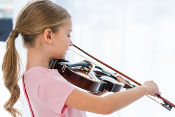 side view of cute little child in pink dress playing violin at home - obrazy, fototapety, plakaty