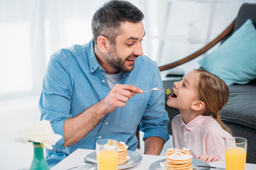 happy father and little daughter having breakfast at home