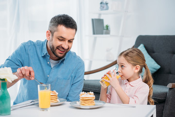 smiling father and little daughter having breakfast at home