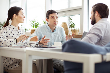 Pleasant meeting. Successful determined young business partners sitting together at the table and having coffee and discussing business