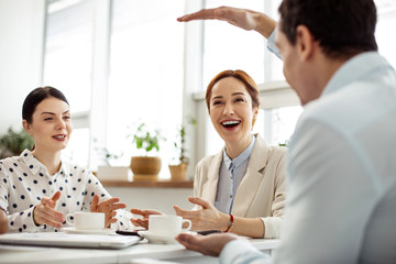 Funny stories. Pretty joyful red-haired young woman laughing and having tea with her friends and they talking