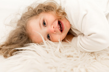 Close-up portrait of lovely baby girl with true exited emotions has fun. Beautiful baby lying on the fluffy carpet and laughing