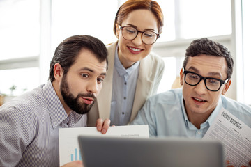 Cam chat. Good-looking alert bearded man having a cam chat with friends and they showing sheets of paper on cam and standing behind him
