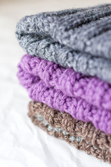 Fototapeta na wymiar A stock of crafted knitted hats of gray, lilac and brown colors on white bokeh background top view