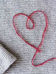 Nice crafting scene: crimson heart pattern made from thread on knitted handmade background