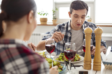 Bon appetit. Handsome concentrated dark-haired man eating a salad and talking and relaxing with his friends