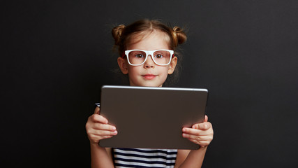 Portrait of smart girl holding digital tablet over black background. Concept of childhood and technology.