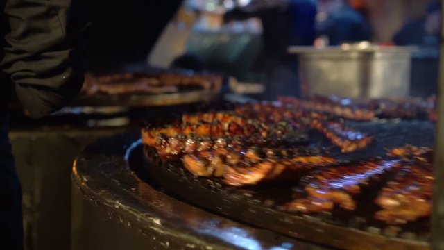 Chef cooking ribs on grill. Male hand holding kitchen stainless steel tongs, appetizing pork ribs on cast iron grill. Restaurant kitchen, cookin