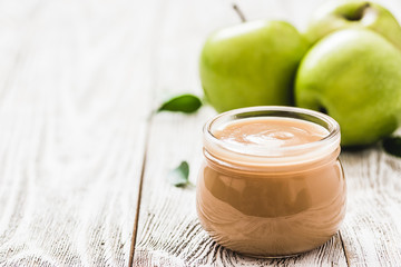 Homemade applesauce in glass jar and green apples on shabby white wooden background. Selective focus, space for text. 