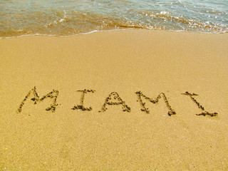 Fototapeta na wymiar Hand drawn word on sand beach in Miami, Florida, USA. Close up detailed image of sand, text and water. Summer vacation and travel concept.